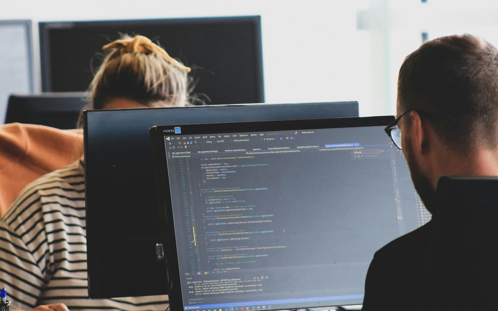 Un programator citește cod sursă pe monitor, într-un birou luminos