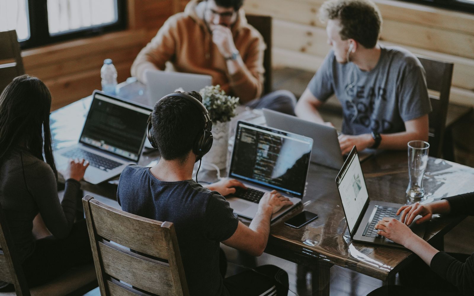 Programatori lucrând împreună la laptopuri, în jurul unei mese de lemn