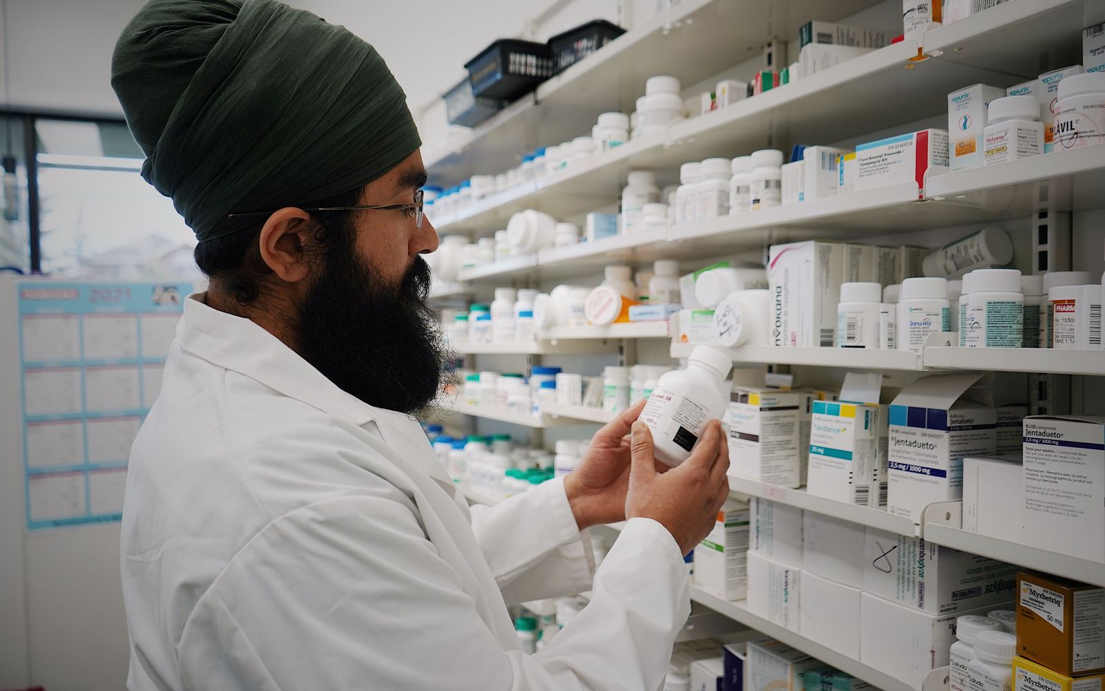 Un farmacist verifică un flacon de medicament în fața rafturilor
